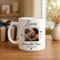 Peut inclure: Mug en céramique blanche avec une anse, orné d'une photo d'un homme et d'un enfant enlacés. Le mug porte le nom "Lucas" en écriture manuscrite, avec le texte "Bonne fête Papa" et "On t'aime fort", ainsi que des cœurs.
