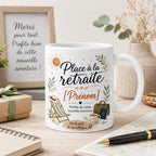 Gros plan du design mug retraite personnalisé avec prénom, message “Profite de cette nouvelle aventure”, feuillages, soleil, transat, sac de voyage et café.