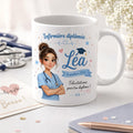 Mug blanc personnalisé pour infirmière diplômée, décoré avec le prénom Léa, un avatar de soignante en tenue bleue et un message de félicitations, présenté sur un bureau avec accessoires médicaux.