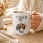 Main tenant un mug blanc personnalisé avec texte et photo de famille, posé sur une table en bois dans une ambiance cocooning beige