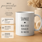 Mug blanc personnalisé avec prénom et texte noir, présenté sur table en bois clair dans une ambiance beige chaleureuse