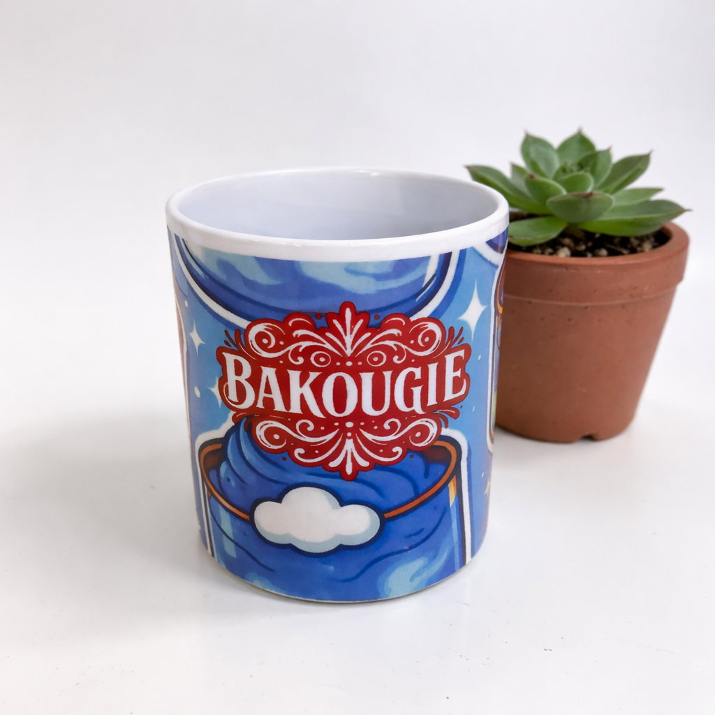 Mug blanc avec decor bleu et logo BAKOUGIE au centre, photographie sur fond clair avec une plante grasse en pot a droite