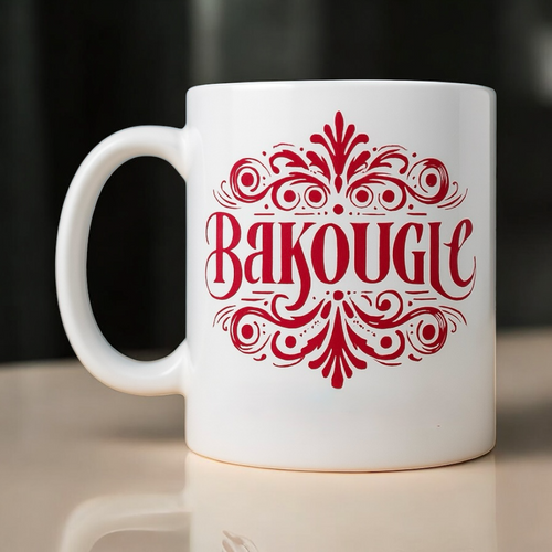 Mug blanc avec anse visible a gauche et logo decoratif rouge BAKOUGIE imprime au centre, pose sur une surface claire devant un fond sombre flou