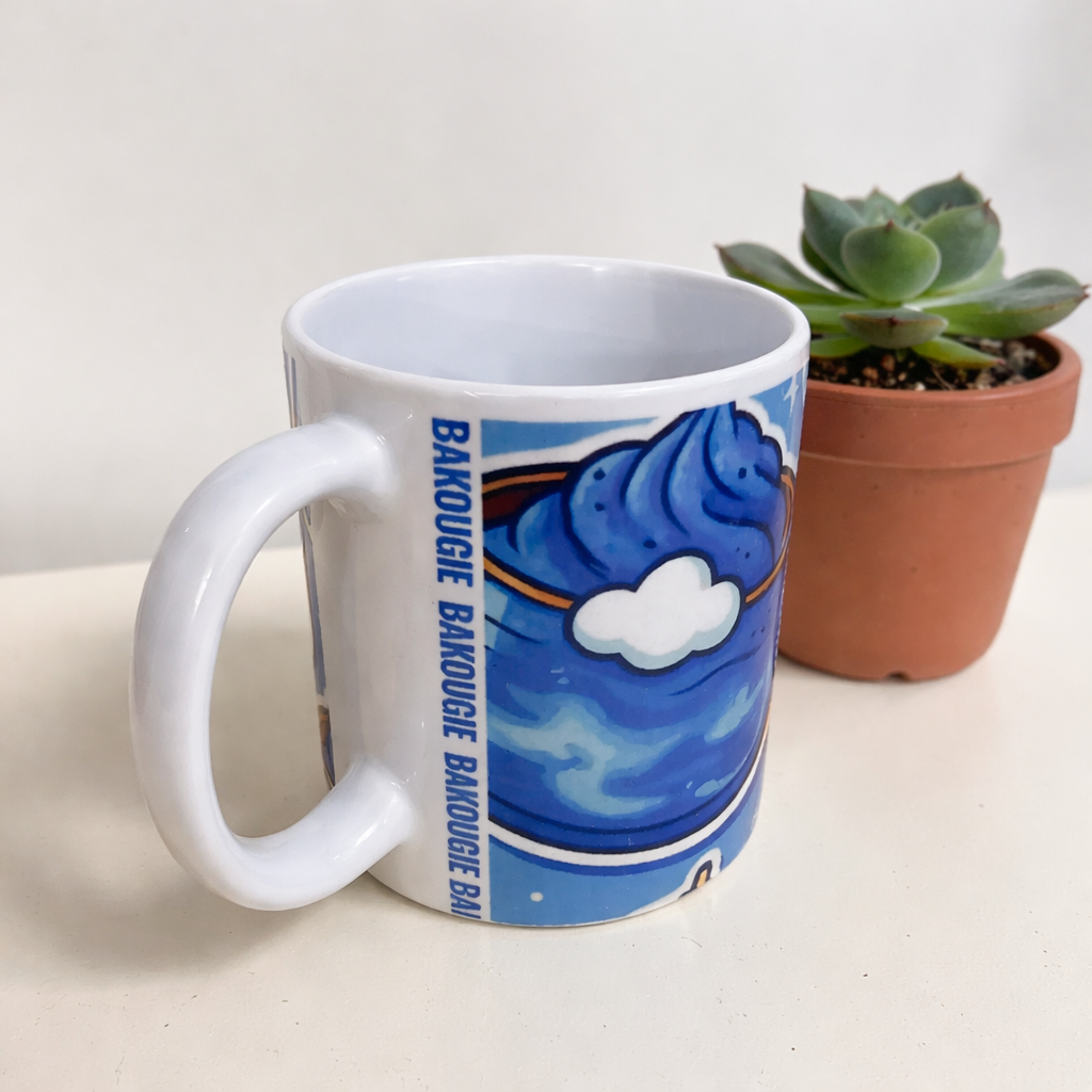 Mug blanc avec decor bleu et nuage blanc, bande verticale BAKOUGIE pres de l anse, photographie sur fond clair avec une plante grasse en pot a droite