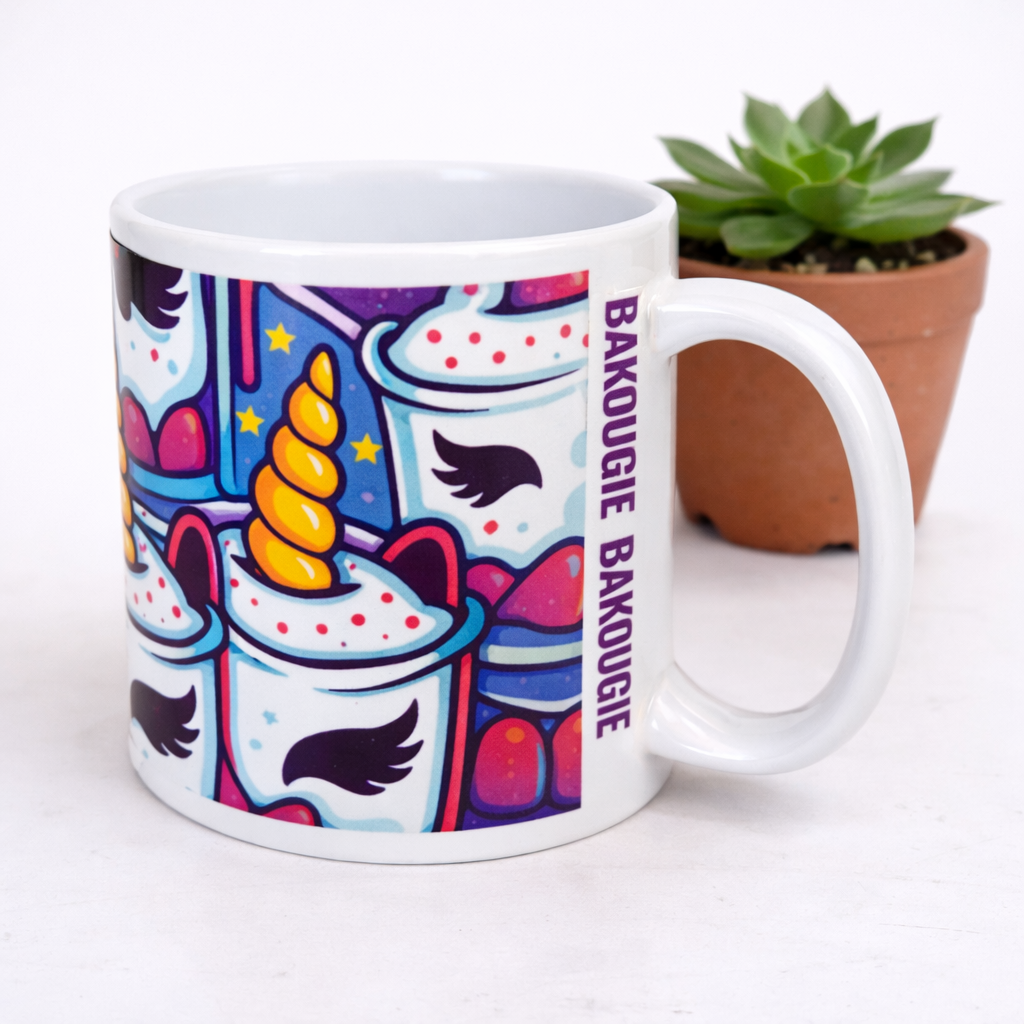 Mug blanc avec illustration colorée de motifs licorne et texte vertical BAKOUGIE, photographié en gros plan devant une plante en pot