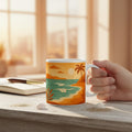 Main tenant un mug blanc avec une illustration de plage tropicale aux tons orange et turquoise, pose sur un bureau clair avec un carnet, un stylo, du sable et des coquillages