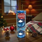 Tumbler blanc avec decor bleu BAKOUGIE et paille metallique, pose sur une table en bois dans une ambiance festive avec pommes de pin, boule rouge, plaid ecossais et lumieres chaudes en arriere-plan