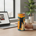 Main tenant un tumbler blanc avec une illustration coloree de chats, pose sur un bureau en bois pres d un ordinateur portable, d une tasse claire, d un pot a crayons et d une plante
