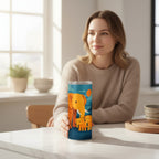 Personne assise derriere un tumbler blanc avec couvercle transparent et illustration coloree d un elephant et de deux petits elephants, pose sur une table claire dans un interieur lumineux