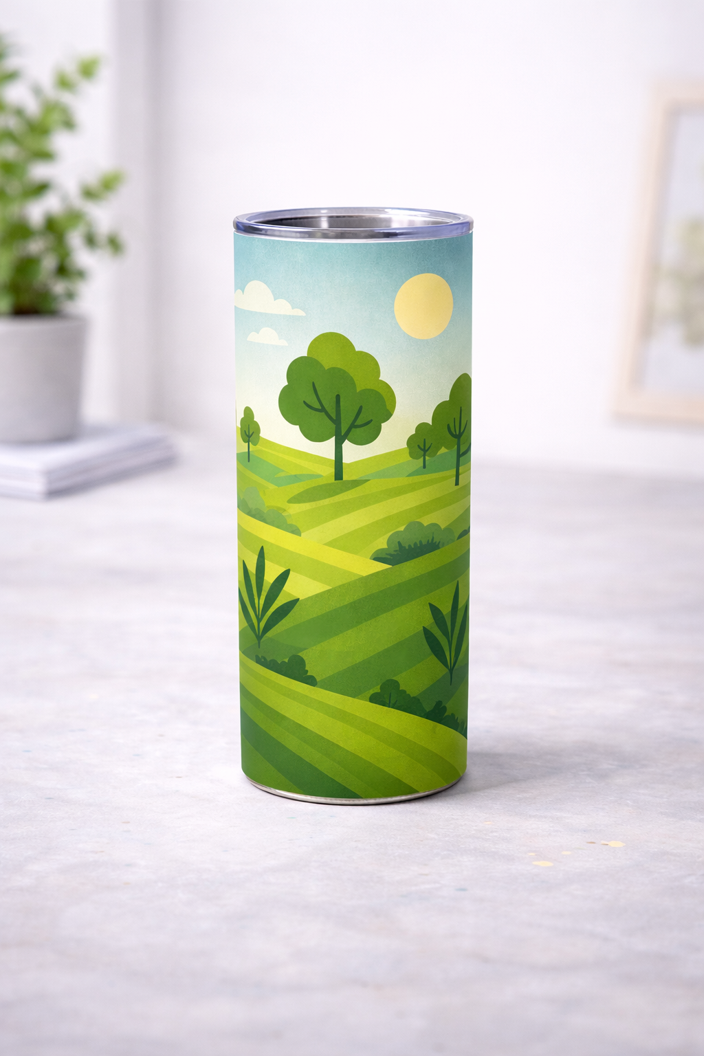 Tumbler haut avec decor illustre de paysage vert, vu de face sur une surface claire, avec collines, arbres, soleil et ciel clair, devant un fond interieur flou
